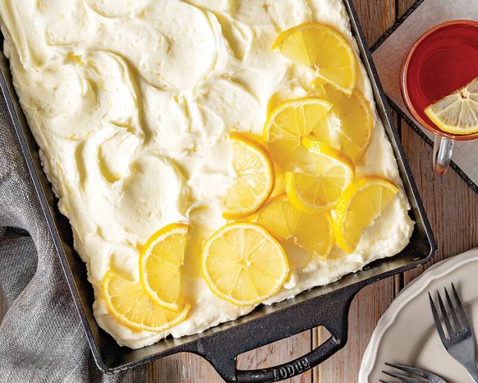 Lemon-Sweet Tea Cake topped with lemon slices, tea in a mug on the side with forks