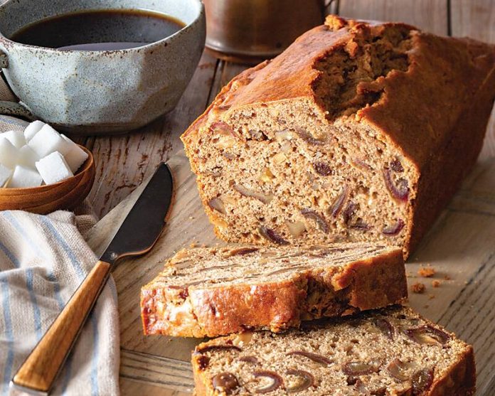 Coffee-Date-Nut Bread, two slices taken out of it and laying on a cutting board, a cup of coffee, bowl of sugar, and serving spatula nearby