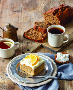 Lemon-Sweet Tea Cake slice with mugs of tea and coffee-date-nut bread sliced in the background