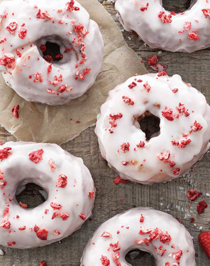 strawberrydoughnut Frosted strawberry doughnuts on baking parchment paper.